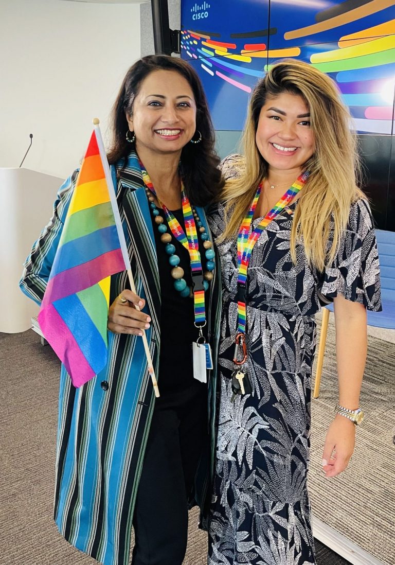 Varsha holding a Pride flag next to a colleague.