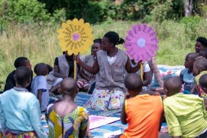 A woman and children sitting in a circle outside during a lesson