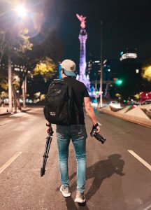 Man with back toward camera wearing backwards hat and Cisco backpack holding camera equipment in downtown Mexico City.