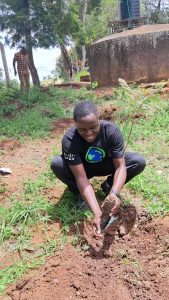 Man wearing all black crouched down in the dirt planting a plant.