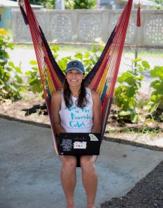 Valerie sitting with laptop in hammock facing camera.