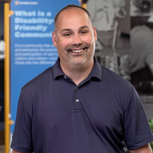 A man smiling for the camera, wearing a purple polo shirt