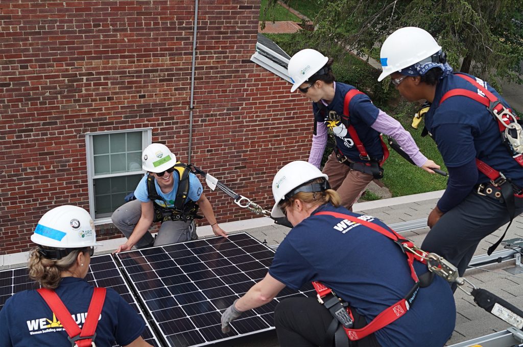 Five young GRID Alternatives AmeriCorps members installing solar panels on top of a building. Image provided by GRID Alternatives