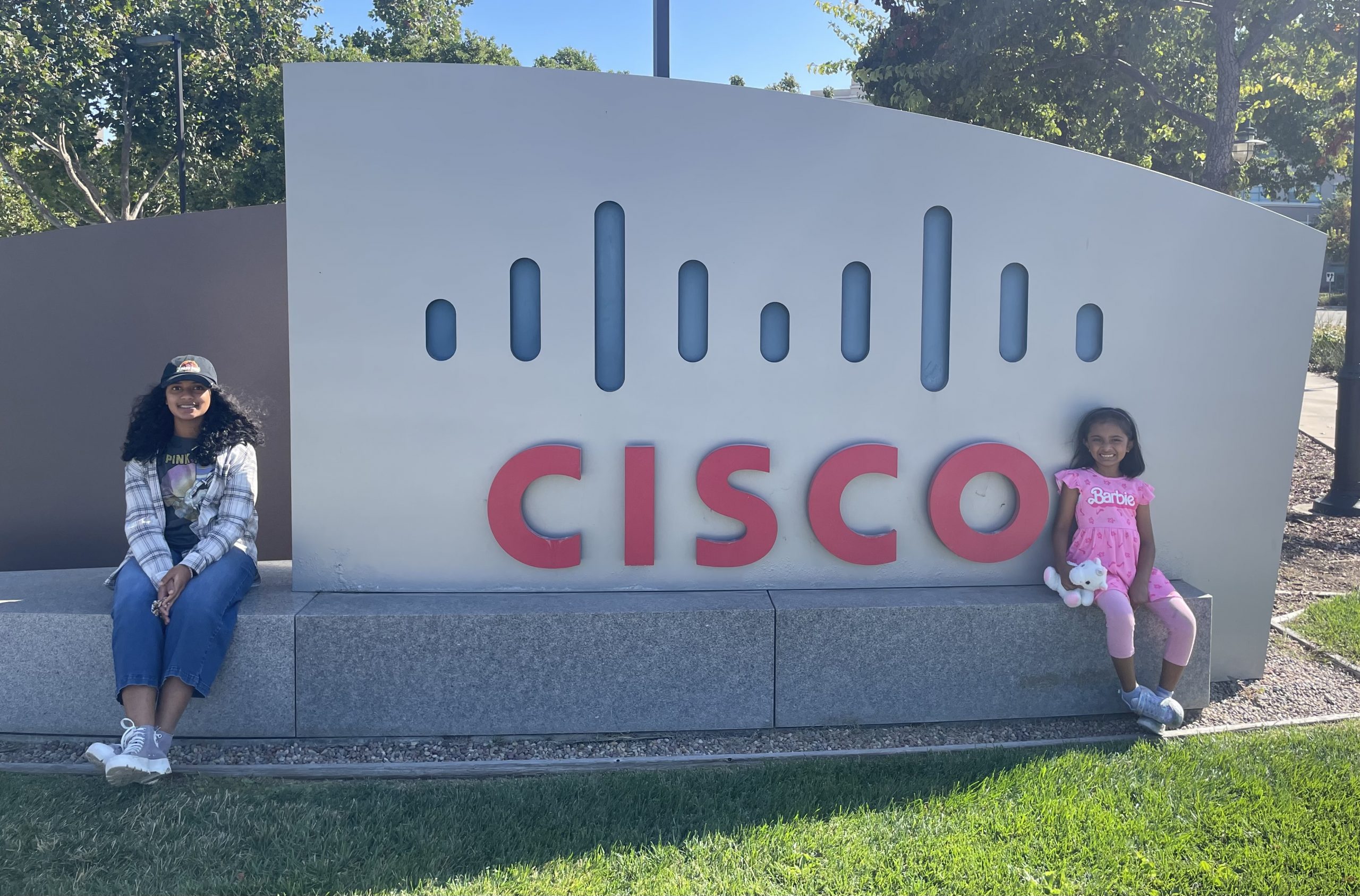 Nitesh's two daughters sitting next to a large Cisco sign.
