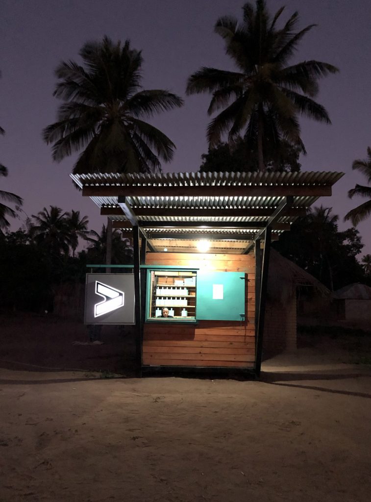 A wooden structure with palm trees behind it, lit up at night.