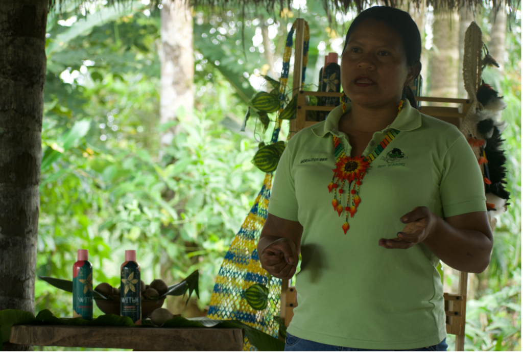A woman wearing a lime green shirt, speaking with a lush green background behind her