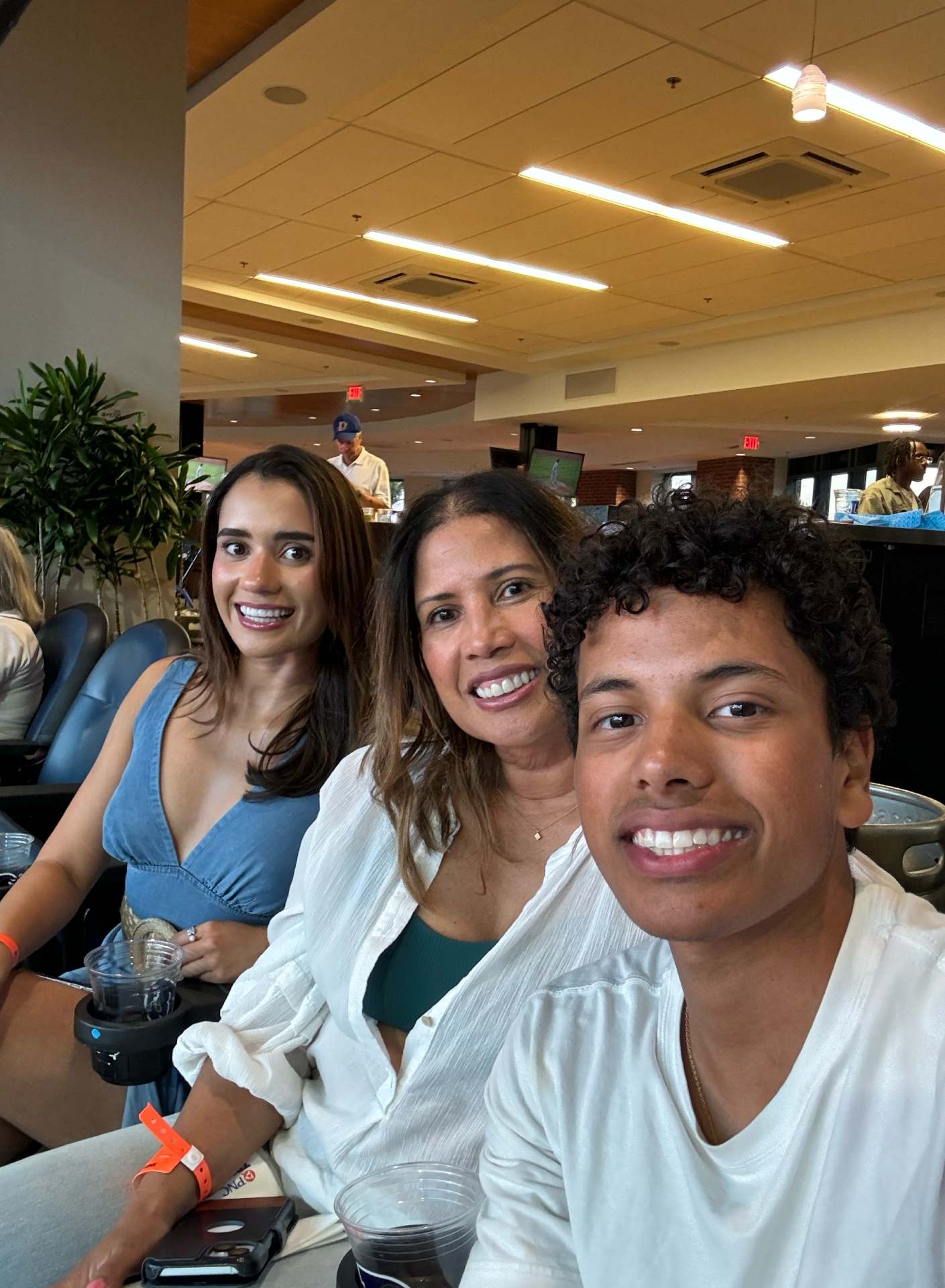 Two women with brown hair and one young man sitting at box seats at an event smiling for a selfie.