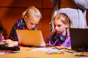 Children sit at a table learning and engaging in code activities.