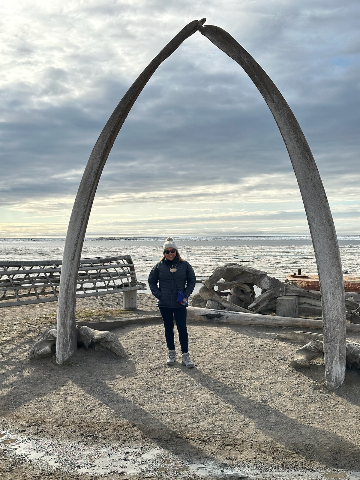 Woman on Arctic beach standing under whale bone arch.