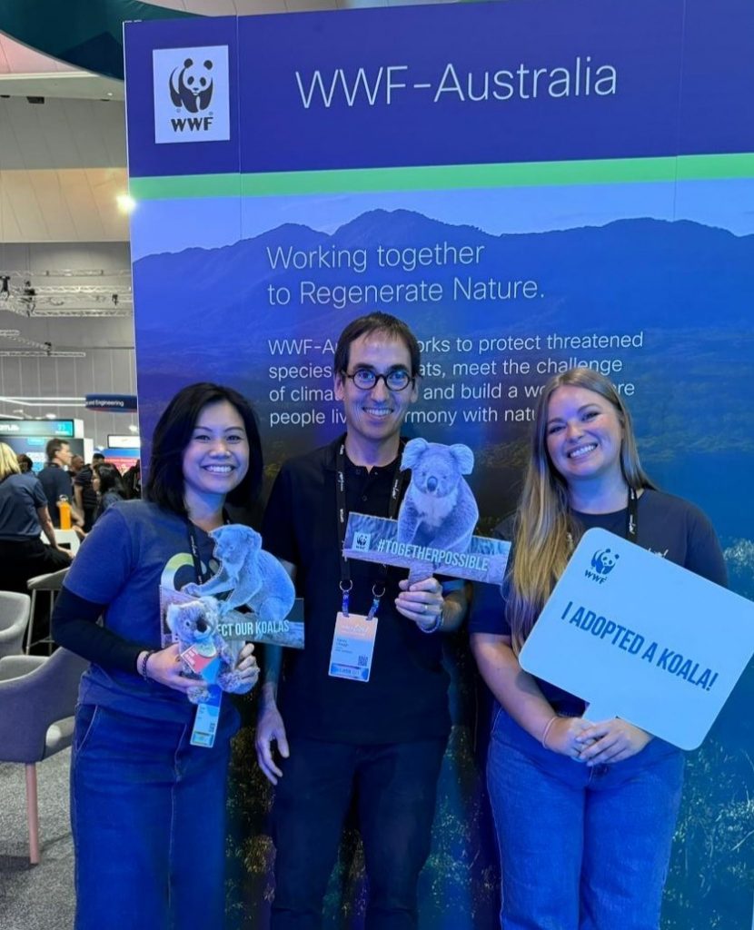 Three people at an event, holding cutouts of koalas and a WWF sign with a Cisco sign behind them