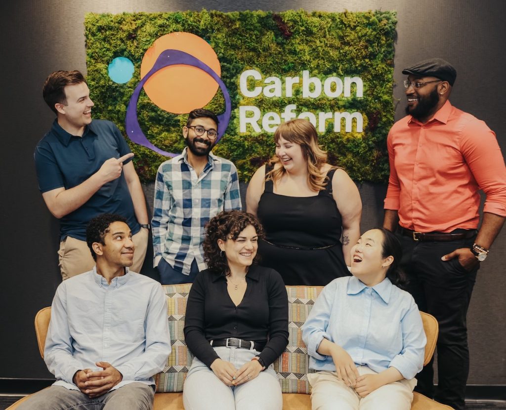 A group of people posing for a photo with a "Carbon Reform" sign in the background