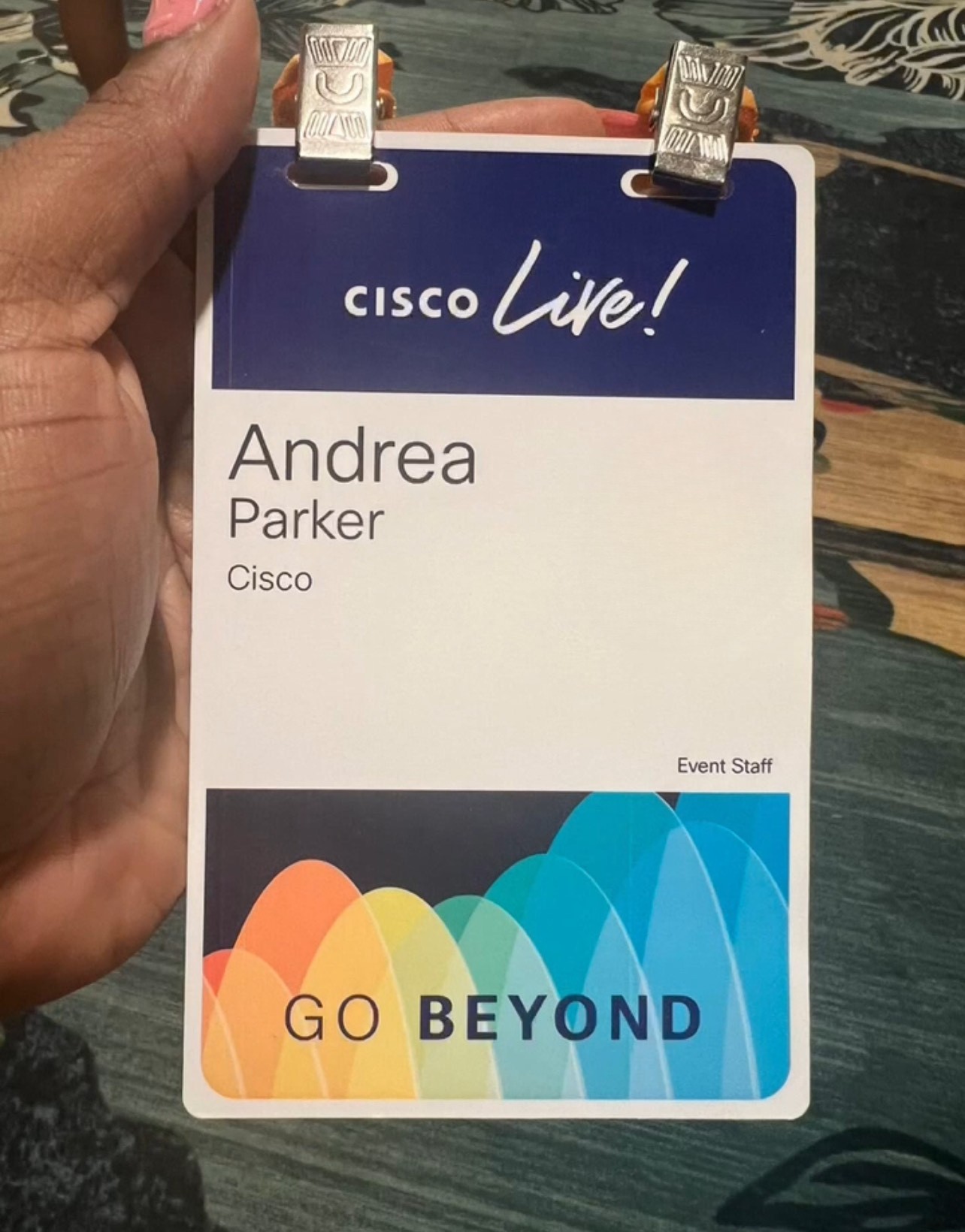 Brown-skinned hand holding Cisco Live badge with attendee's name on it.