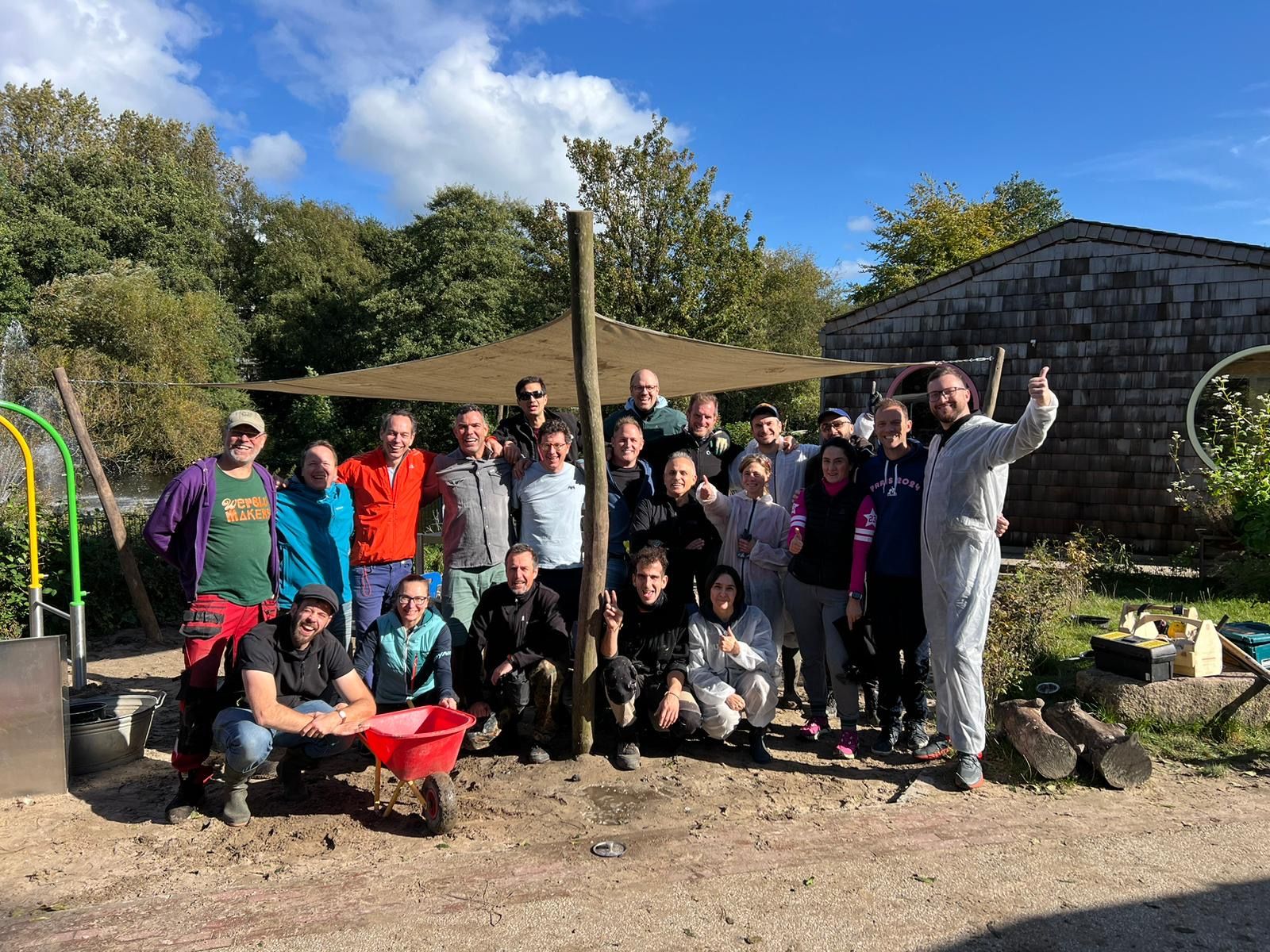 Group of people standing outside in a garden with a red wheelbarrow at a cleanup event.