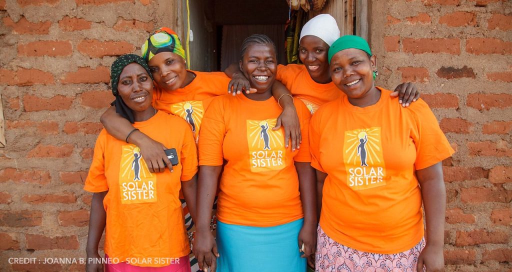 Five women in a warm embrace wearing bright orange t shirts
