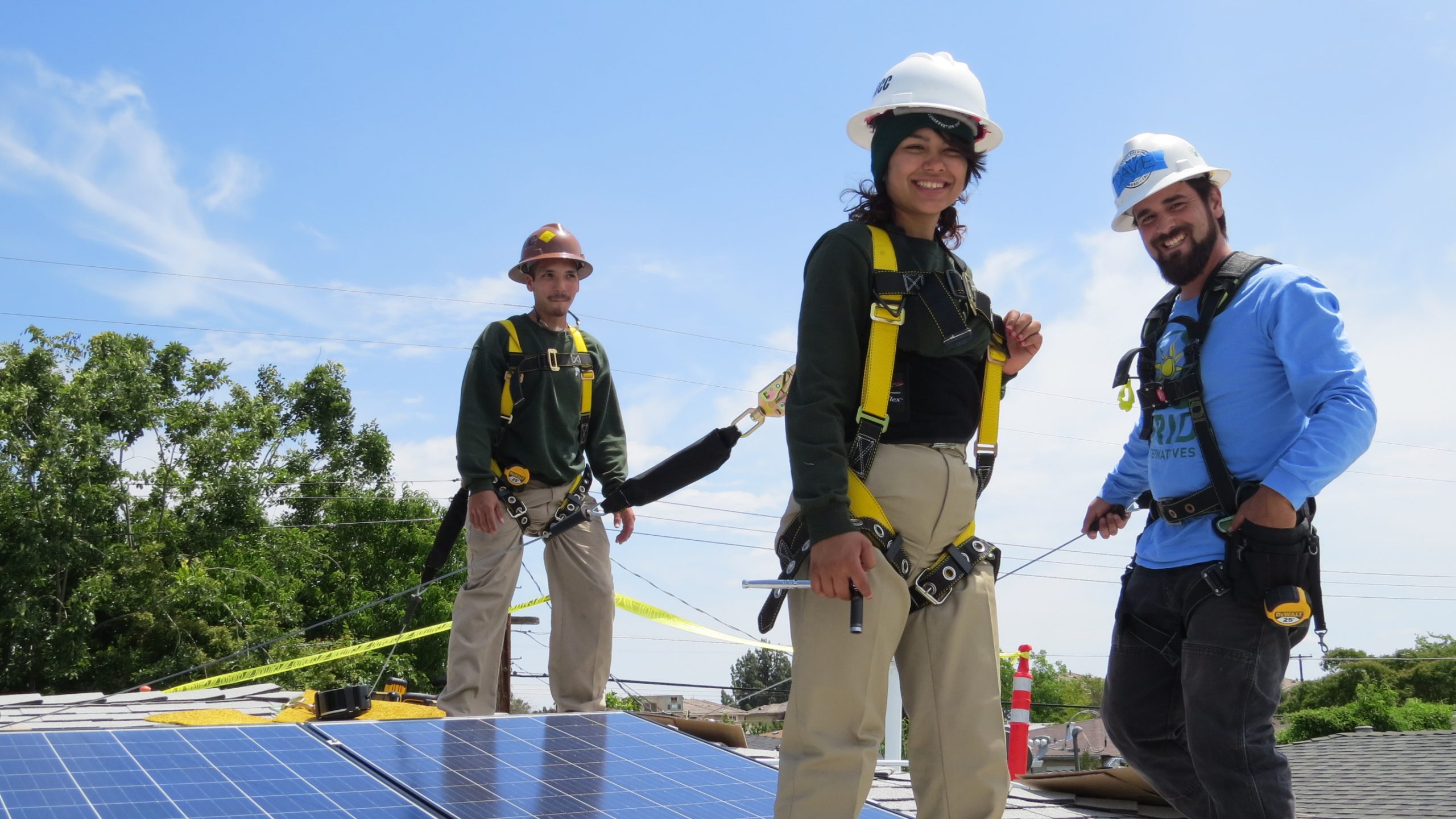 Three people wearing hard hats installing solar roof panels