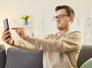Man with glasses squinting while looking at his cell phone at arms length 