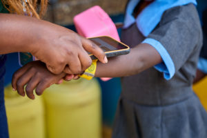 Scanning a colorful Tap2Eat NFC wristband to access a nutritious meal at school.