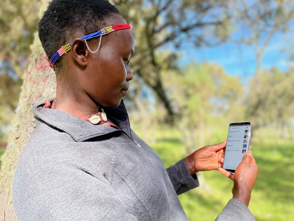 A woman wearing a gray shirt and a colorful accessory, using a cell phone.