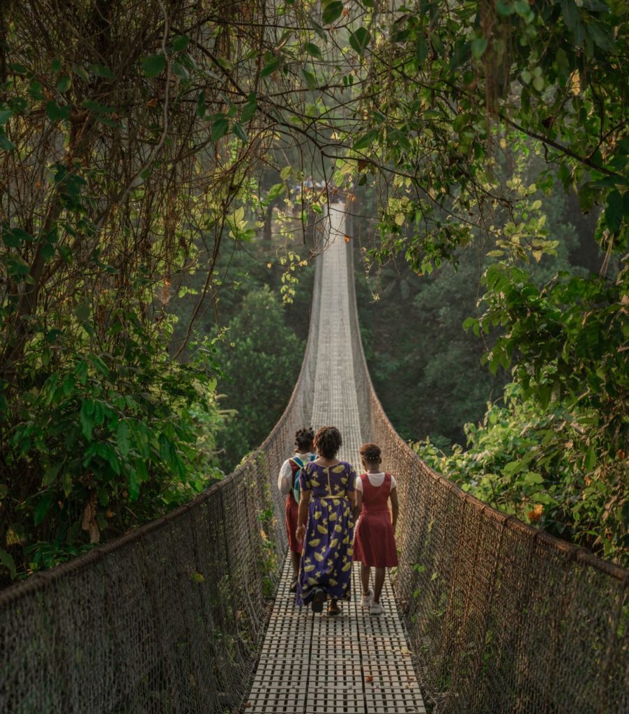 Vertical image of 3 women walking over a bridge in lush vegetation