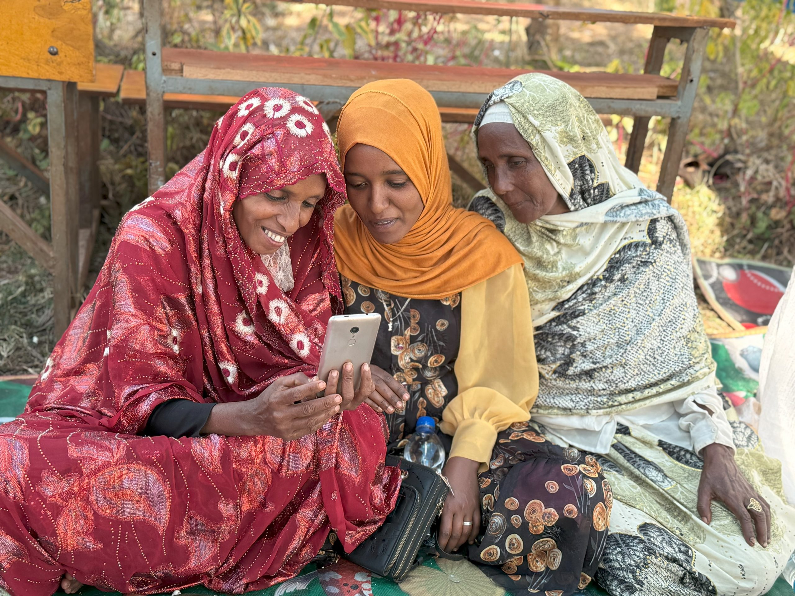 A group of three women, in red, orange, and green, looking at a phone together.