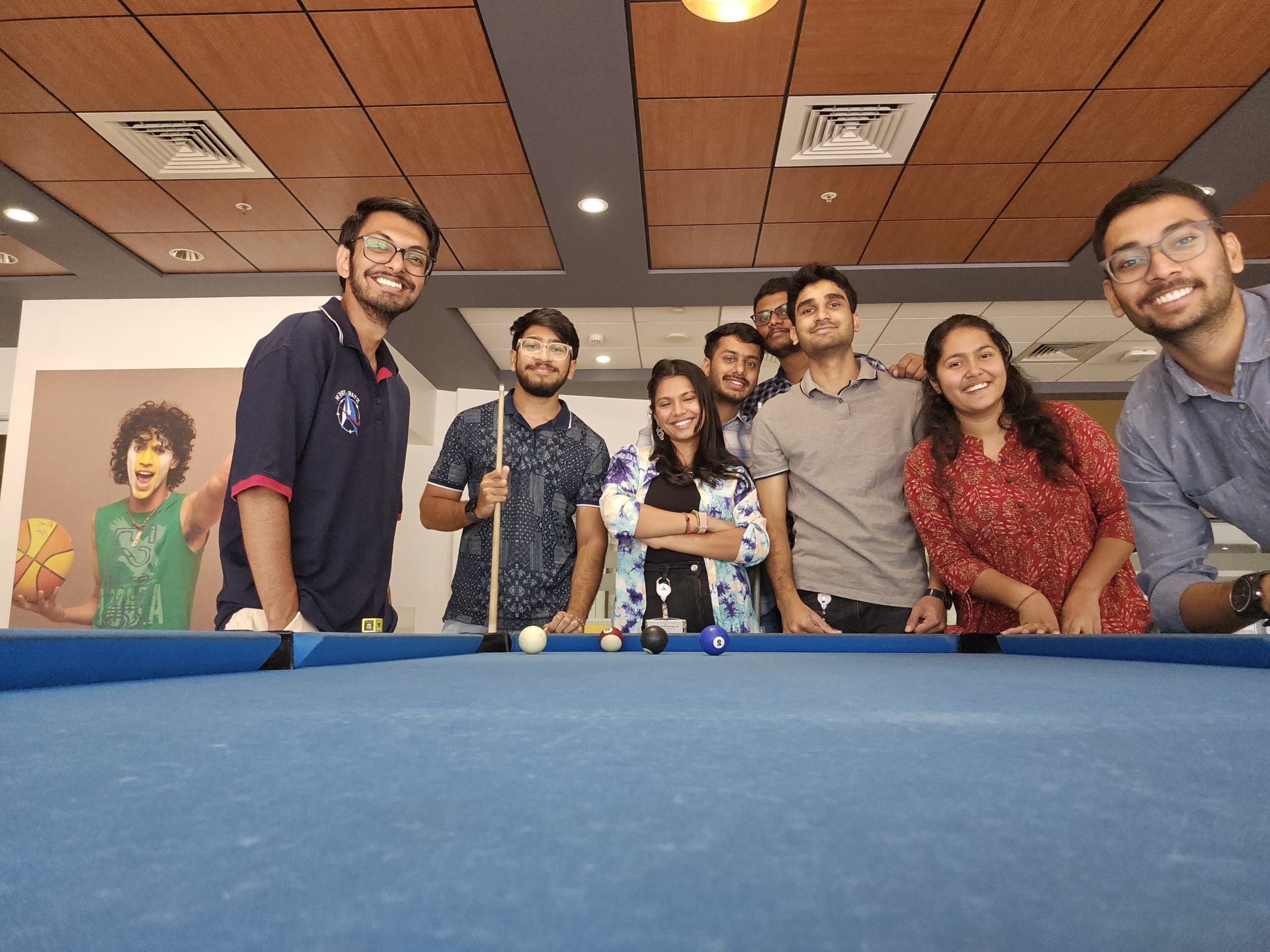 A group of co workers standing together at a pool table smiling.