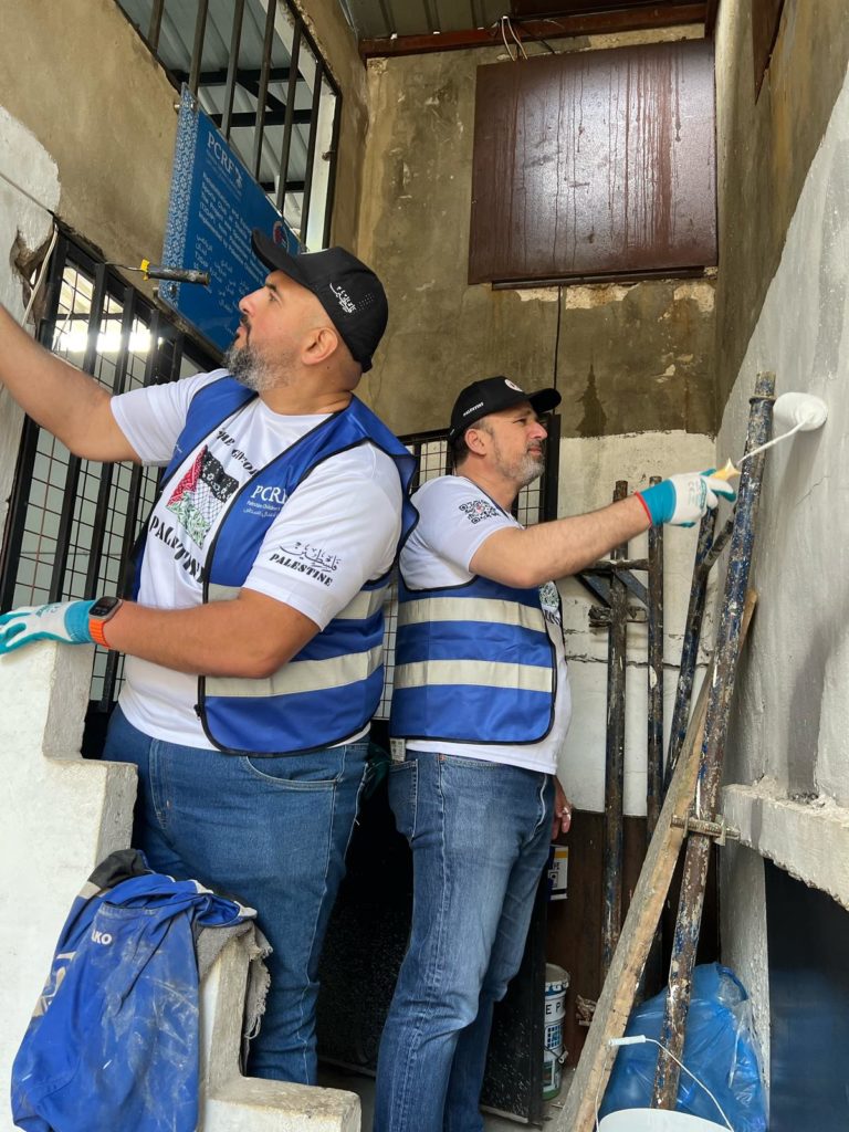 Two volunteers in Time2Give shirts painting a wall at a refugee camp.