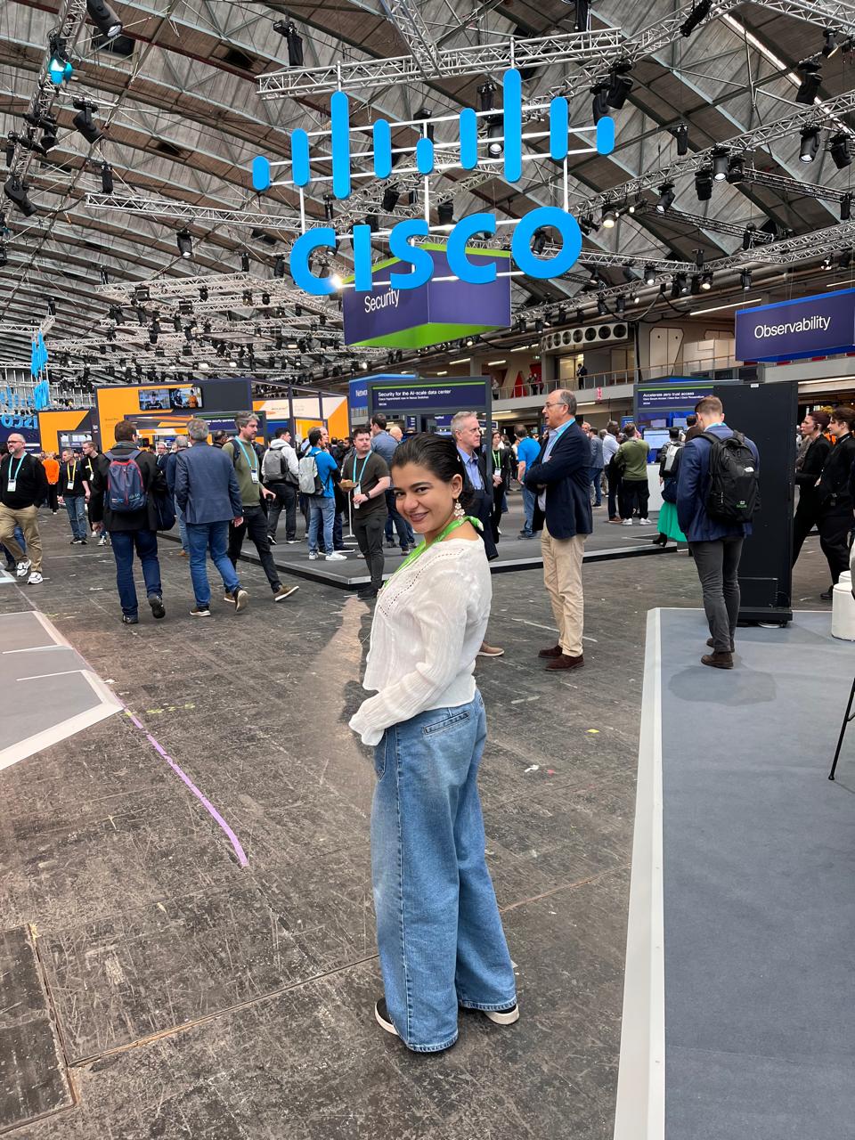 Women standing in a front of a large Cisco sign hanging from the celing of a big conference area.