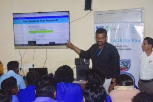 Um instrutor, parado na frente de uma sala de aula cheia de alunos, aponta para uma tela que diz: "Quão forte é a sua senha?" como parte de uma lição sobre segurança cibernética.