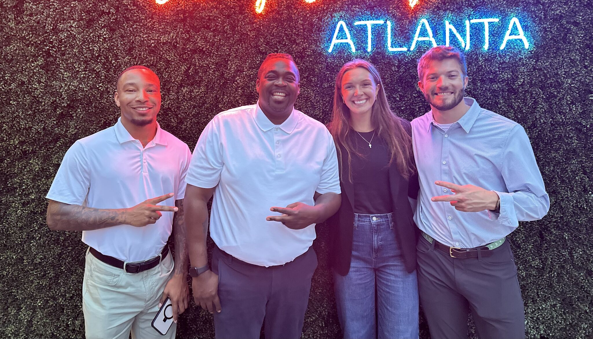 Four people standing in front of a neon Atlanta sign smiling.