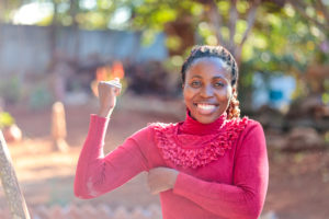 A smiling woman in a red ruffled top makes a fist, standing outdoors in natural light.