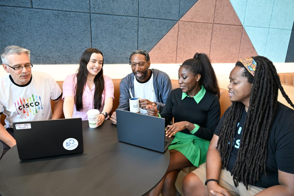 Group of five employees sitting in a booth with laptops open 