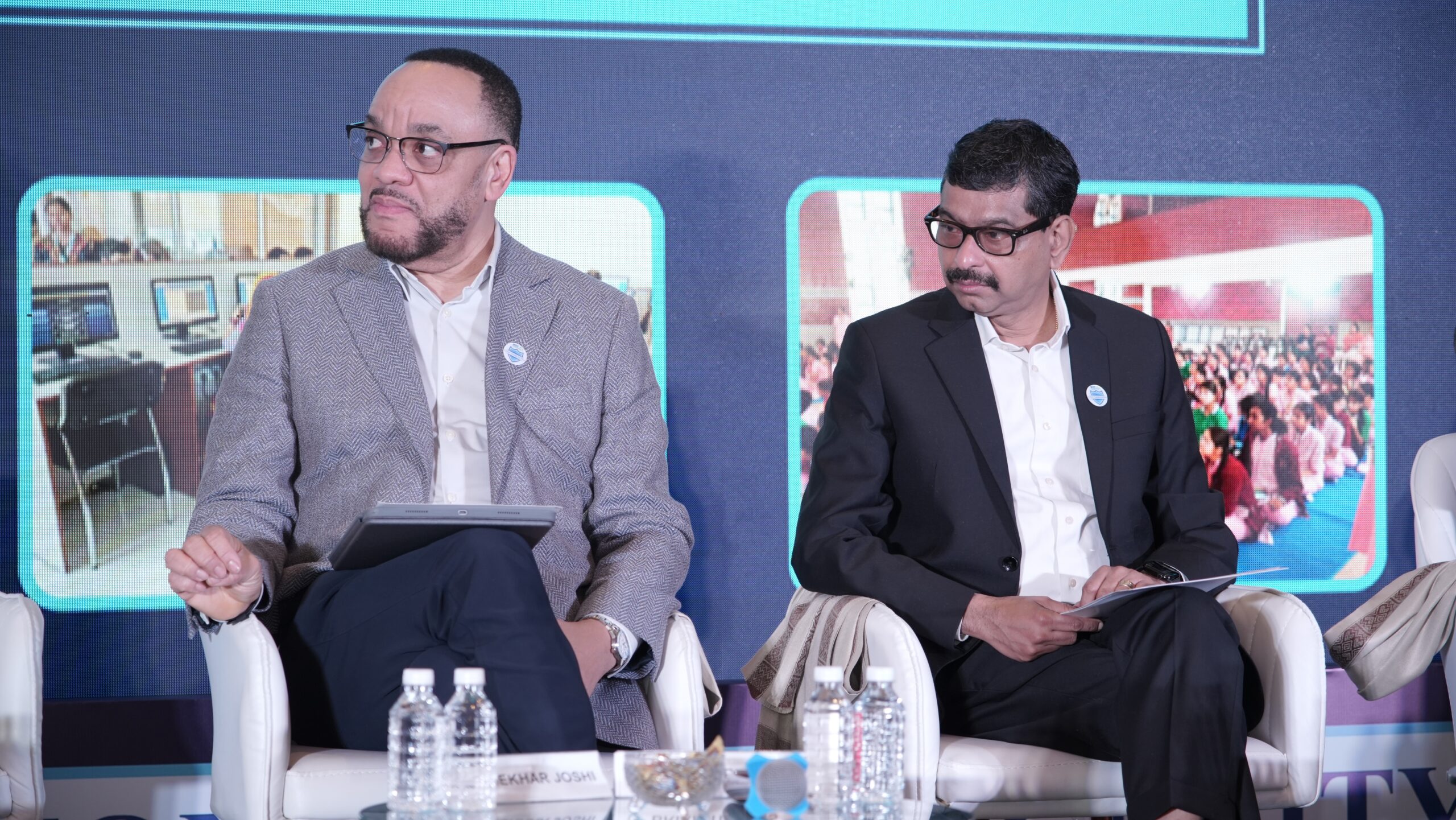 Two men in suits sit on a stage during a panel event in Mumbai, India.