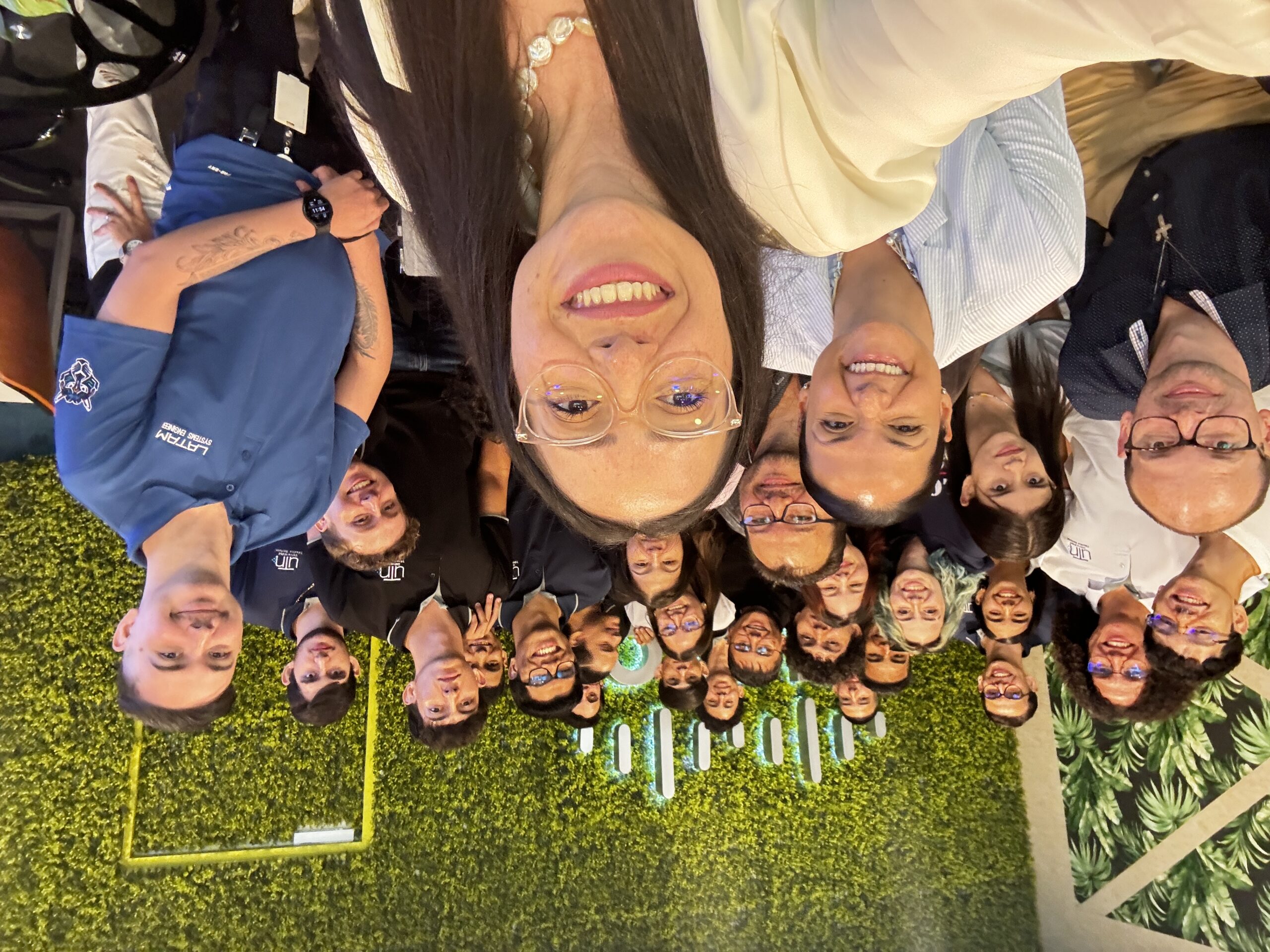 A large, diverse group of smiling students and professionals pose for a cheerful group selfie in front of a Cisco green wall logo, creating a lively and welcoming team photo.