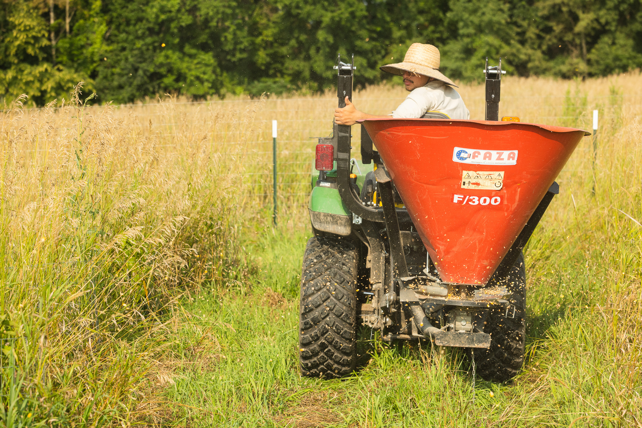 An orange farm vehicle driven by a person with a hat.