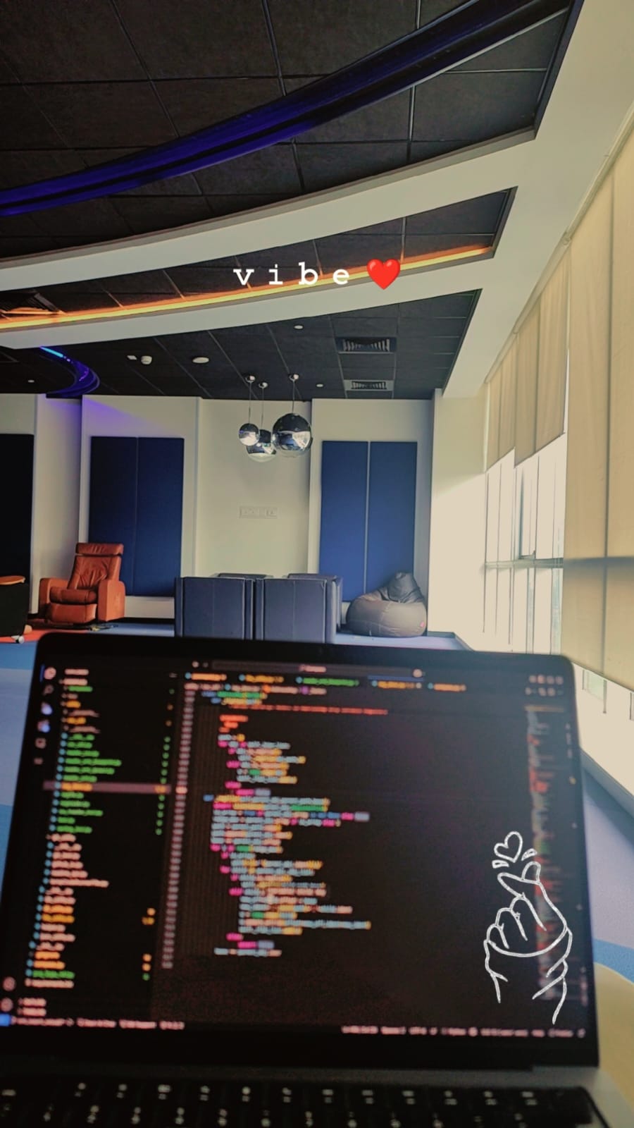 Close up of laptop screen with blurred code. There is an office scene in the background and "vibe ❤️" is overlaid on the screen