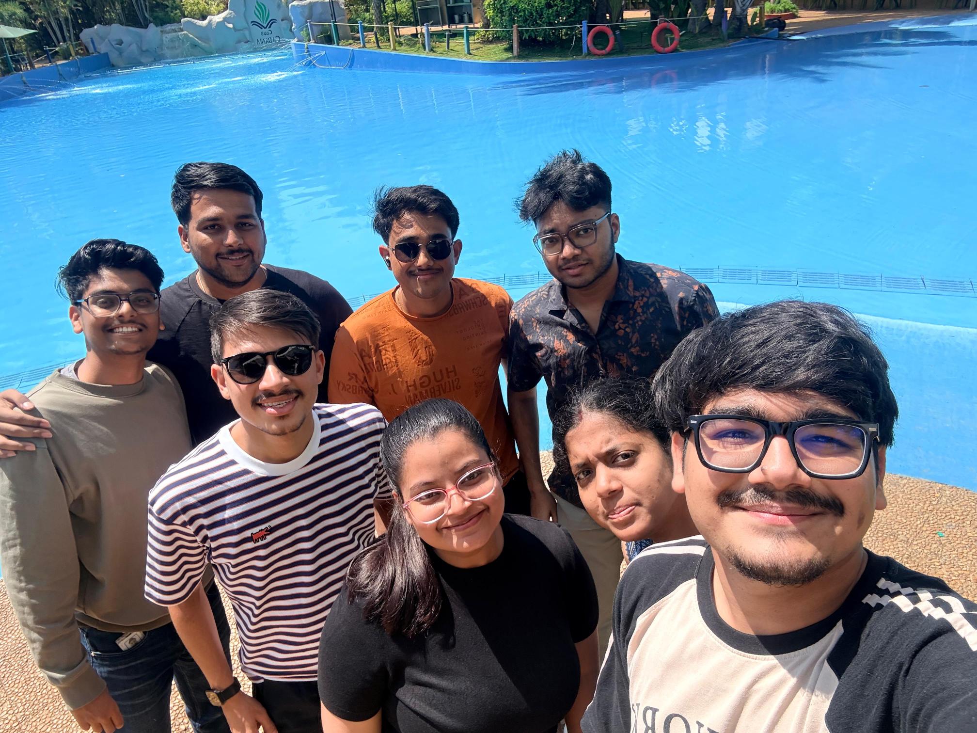 A group of young men and women take a selfie standing in front of a blue pool.