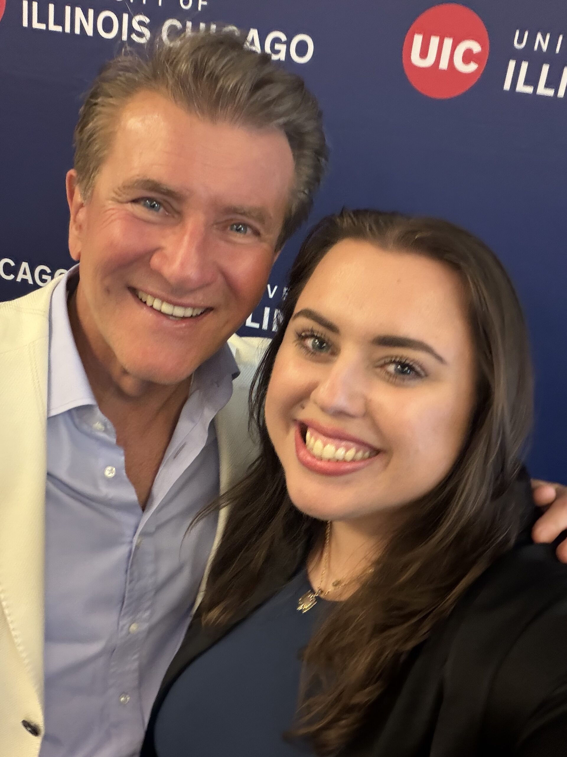 Smiling selfie of a woman and a man at a University of Illinois Chicago event, standing in front of a UIC-branded backdrop.