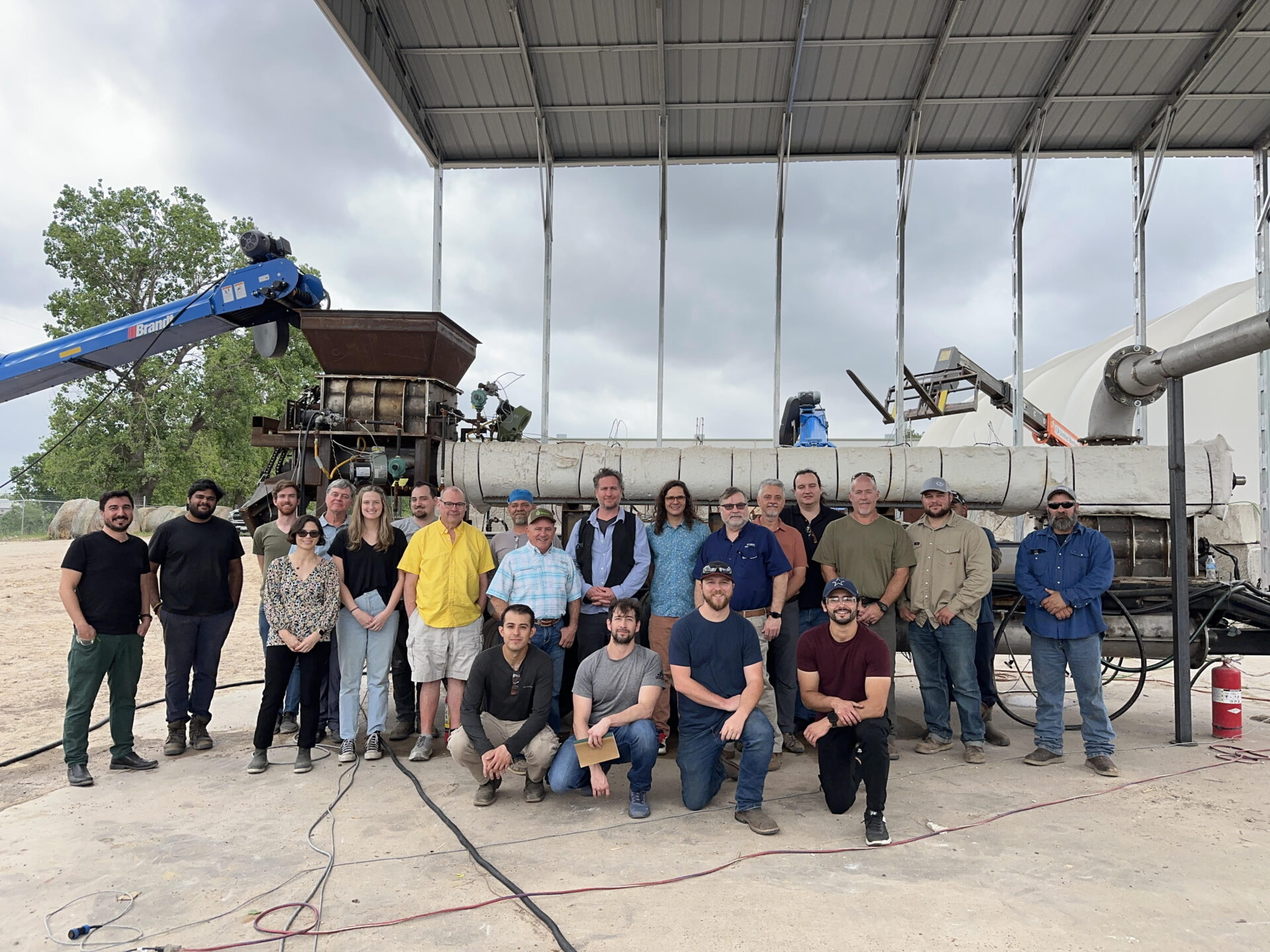 A group of people standing in front of farm equipment in a rural setting.