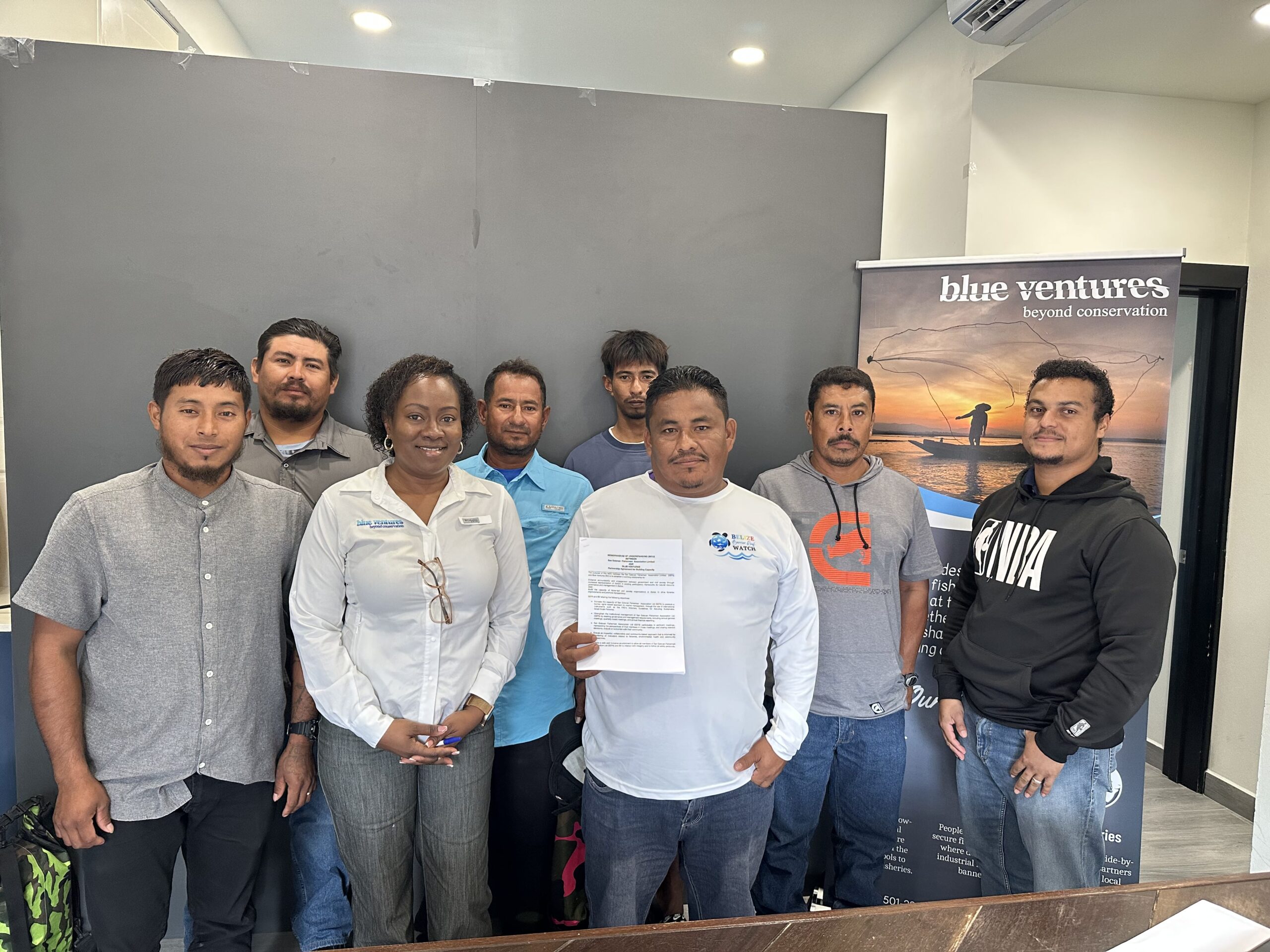 A group of people standing together in an office setting, holding up a piece of paper.