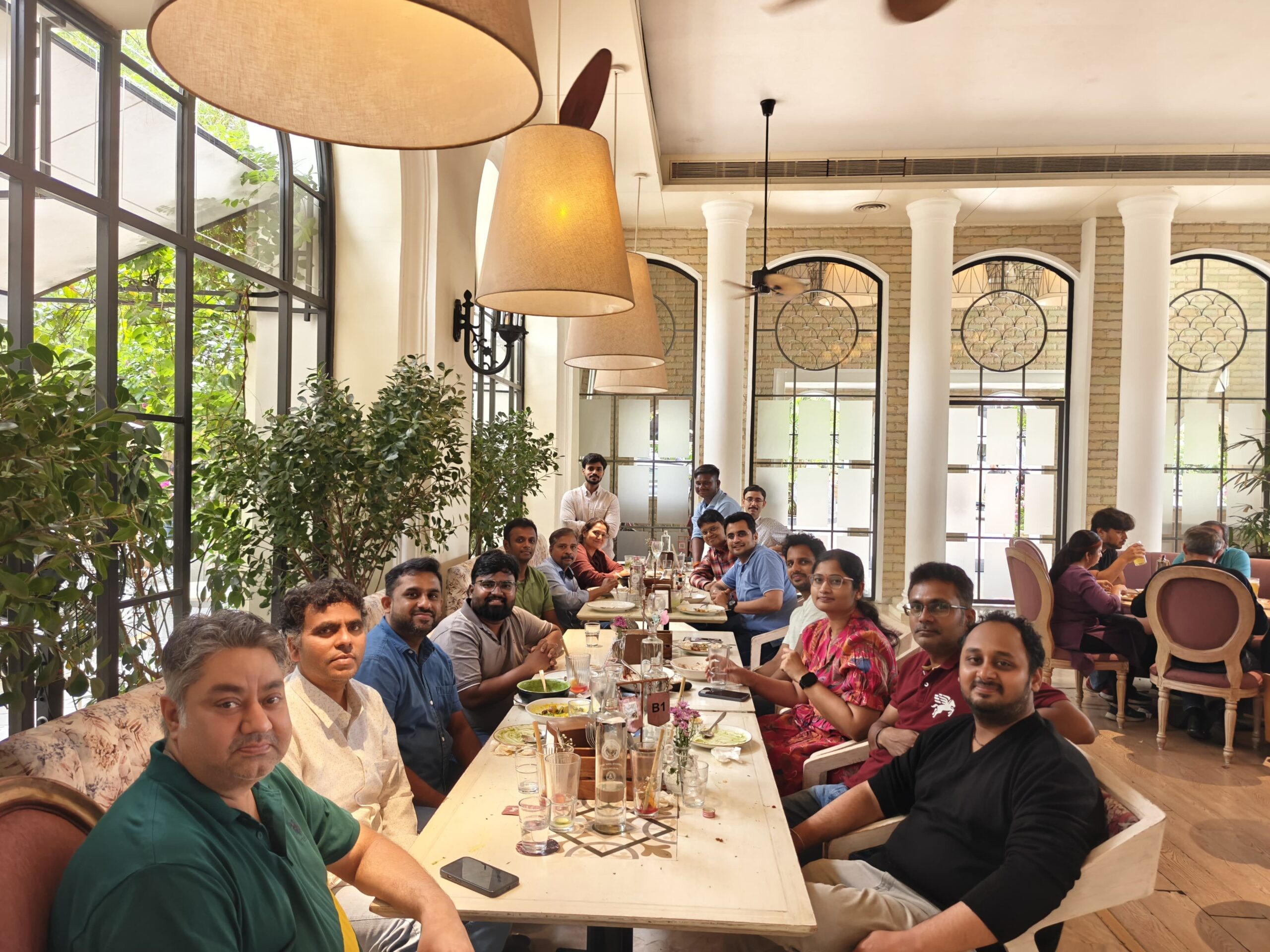 Team members seated together at a long table enjoying a group lunch in a bright restaurant. 