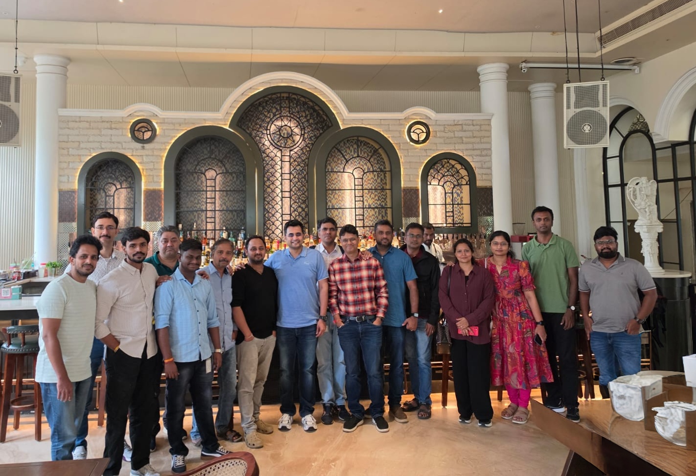 Team group photo standing inside a bright restaurant with arched windows and a decorative bar backdrop.