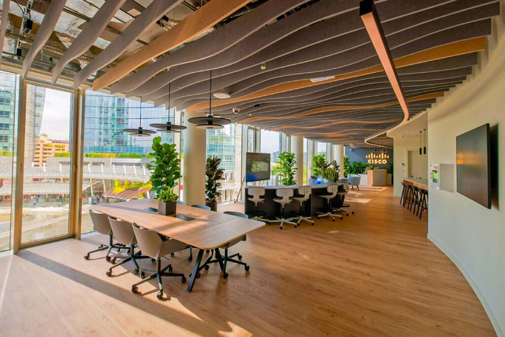 Milan.jpg: A bright, open-plan office in Milan featuring a unique wave-patterned ceiling, a large wooden conference table, and floor-to-ceiling windows with a city view.