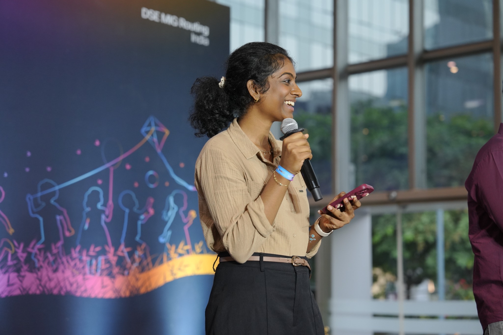 An event host speaks into a microphone while holding a phone, with a colorful DSE FamZilla backdrop behind her.