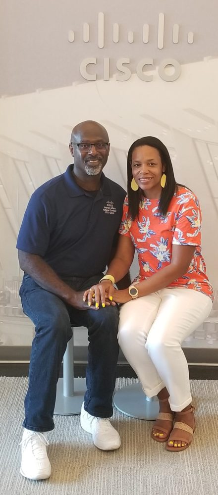 Shawnita and her husband Vanis smile under a Cisco logo.