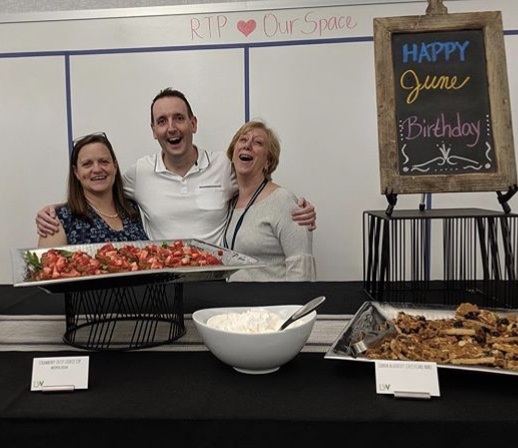 Jeff and two of his peers standing with food and signage for the Workplace Resources monthly birthday party.